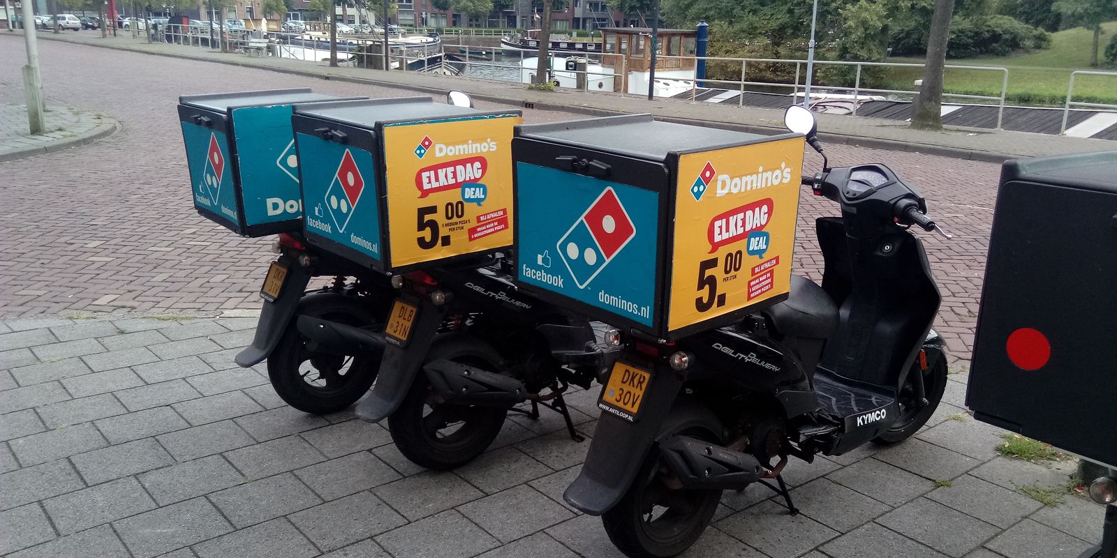 A row of pizza delivery scooters parked outside a shop